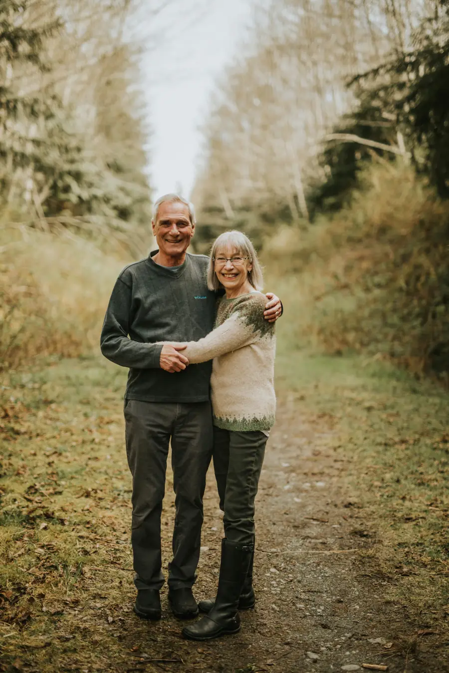 Bill and Donna Mackay stand together on a forest path, holding hands.