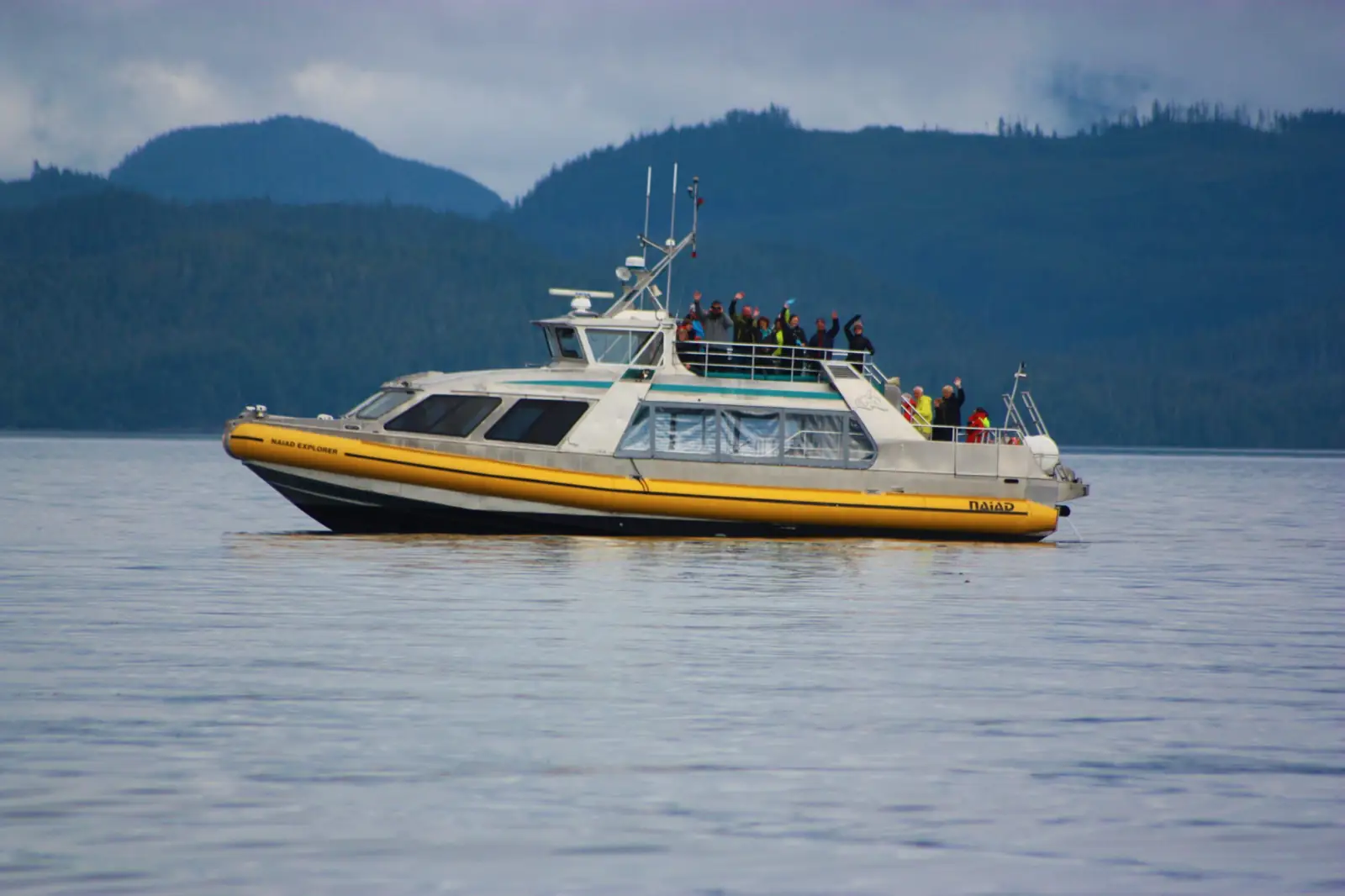 Passengers line the rails of the Naiad Explorer as it cruises beneath coastal mountains.